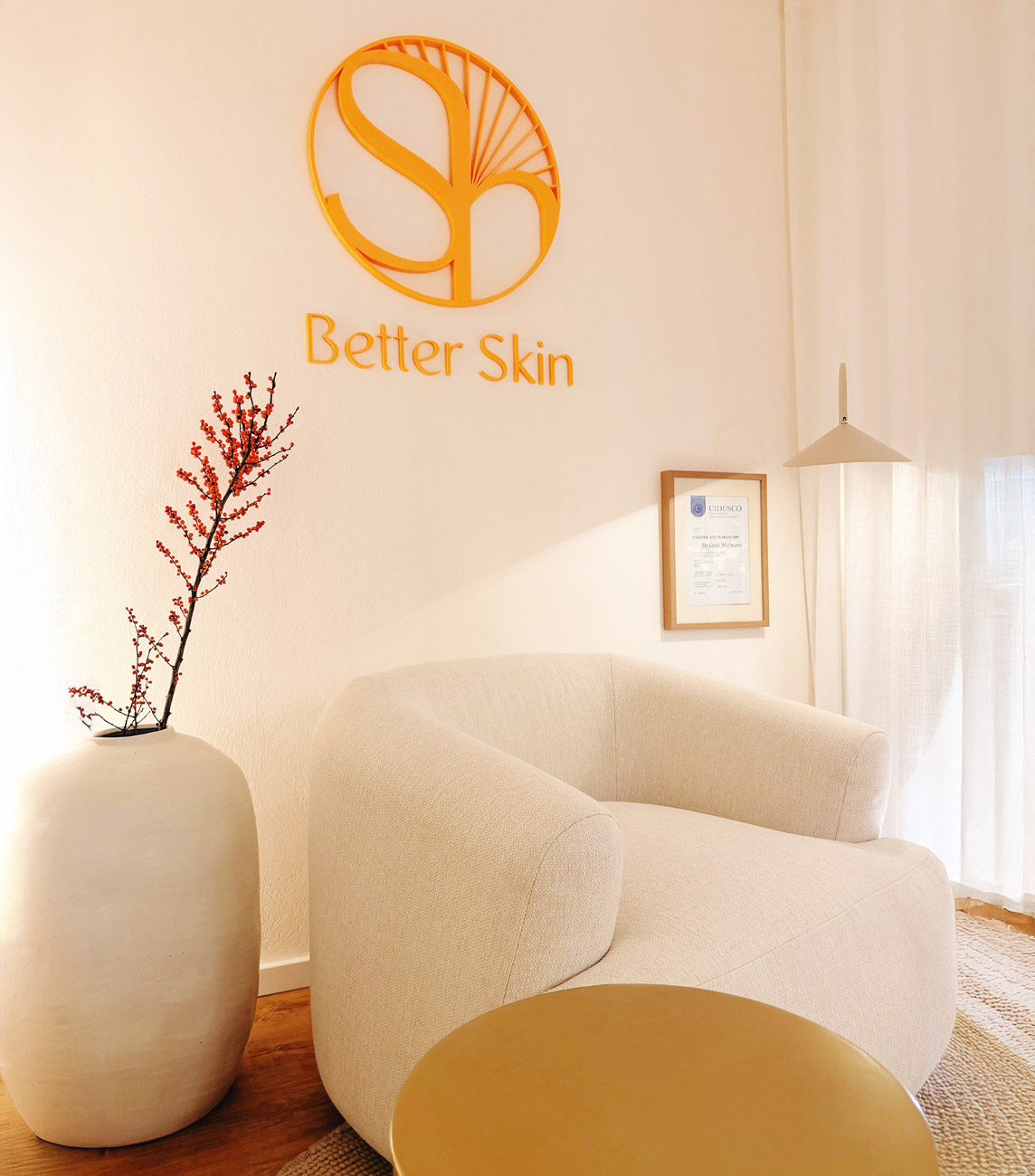 Heller Wartebereich mit beigem Sessel, Vase mit roten Zweigen, Better Skin Logo und Zertifikat an der Wand​​​​​​​​​​​​​​​​​​​​​​​​​​​​​​​​​​​​​​​