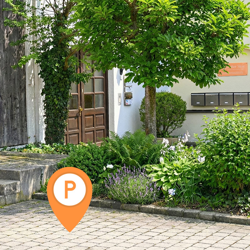 Holztür, grüne Pflanzen und Briefkästen vor einem Gebäude in Ismaning mit Parkplätzen im Vordergrund​​​​​​​​​​​​​​​​​​​​​​​​​​​​​​​​​​​​​​​​​​​​​