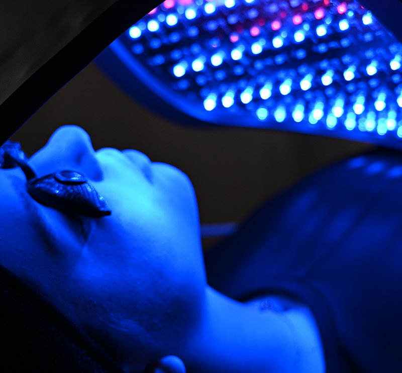 Nahaufnahme einer Person mit Schutzbrille bei Celluma Lichttherapie in dunkler Umgebung mit blauem Licht​​​​​​​​​​​​​​​​​​​​​​​​​​​​​​​​​​​​​​​​​