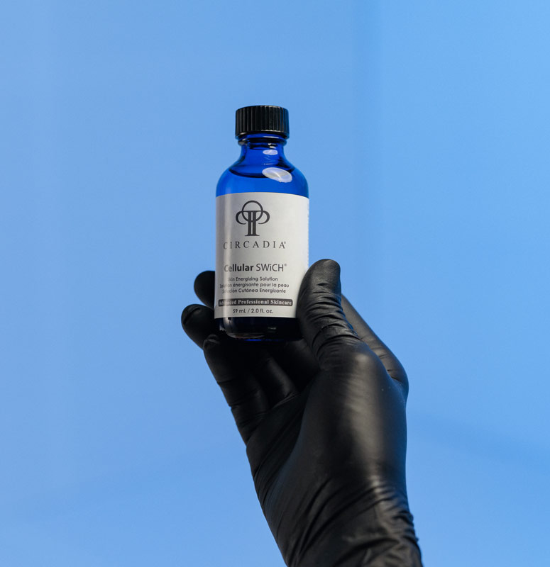 Schwarze Hand mit Handschuh hält blaue Circadia Cellular Swich Flasche vor blauem Hintergrund​​​​​​​​​​​​​​​​​​​​​​​​​​​​​​​​​​​​​​​​​​​​​​​​​​​​